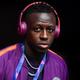 Benjamin Mendy stands in front of a black background wearing orange and purple Beats headphones that match his team jacket.